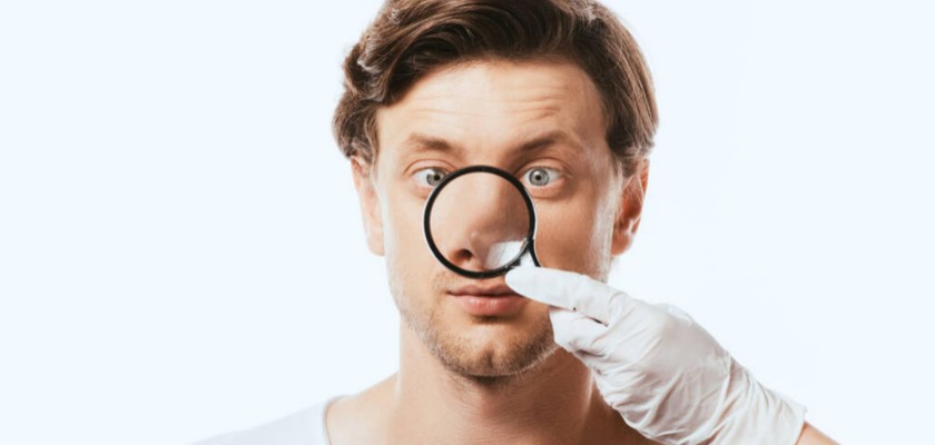 Dermatologo che analizza il naso di un uomo con la lente di ingrandimento