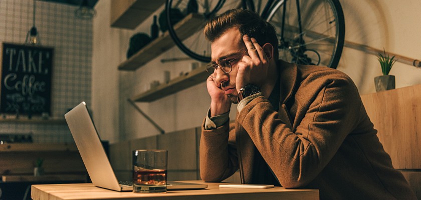 Uomo con gli occhiali con lo sguardo stressato e i gomiti appoggiati sul tavolino mentre fissa il monitor del suo Notebook